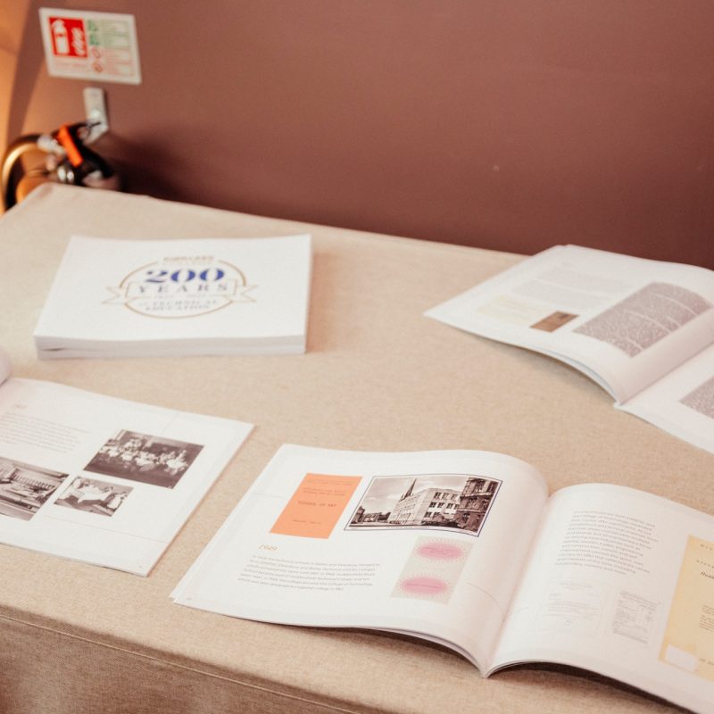 A table displays a book and brochures celebrating a 200-year anniversary, featuring historical images and text.