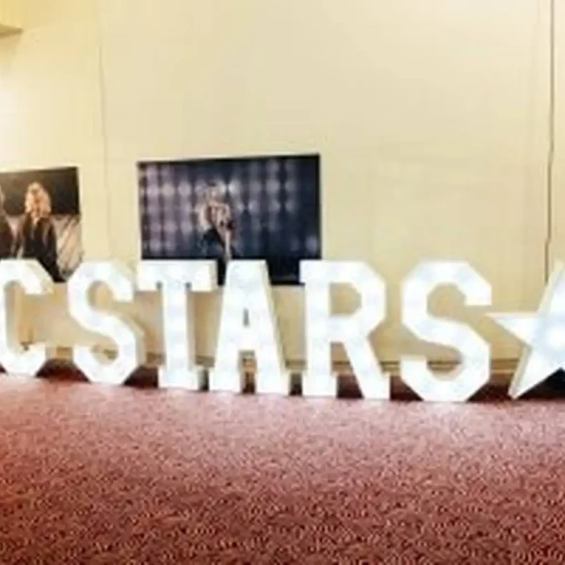 Illuminated KCSTARS letters and framed photos on a carpeted floor, likely in a college setting for a student event or performance showcase.