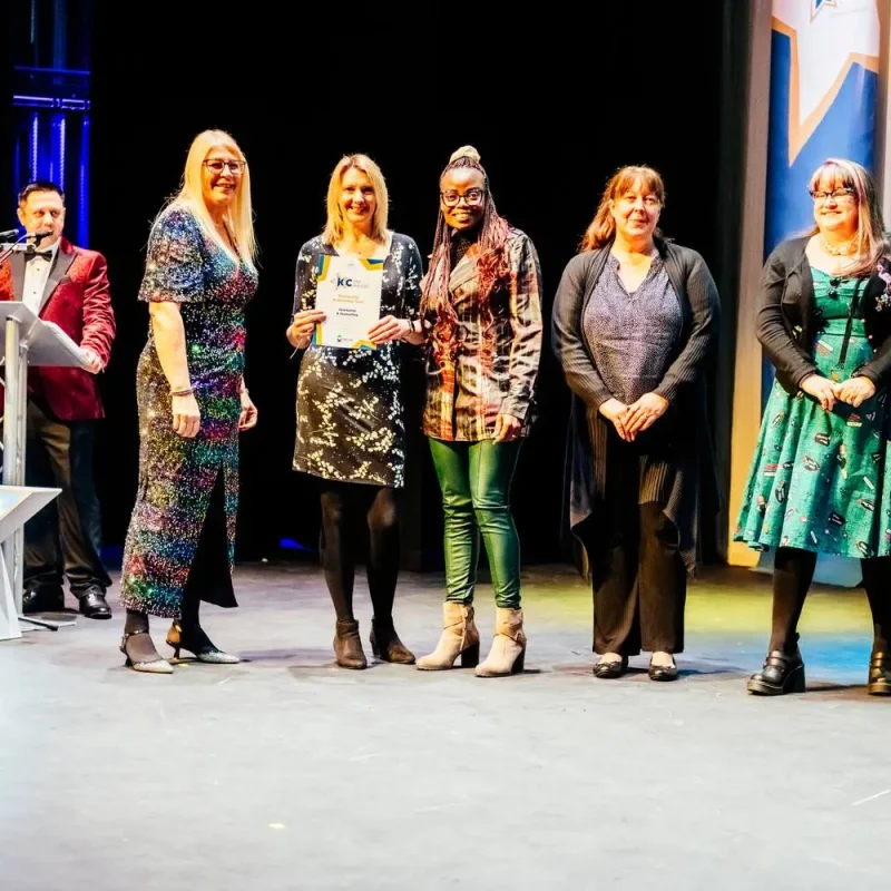 A group of five people on a stage, one holding a certificate, with a podium and a large star decoration.