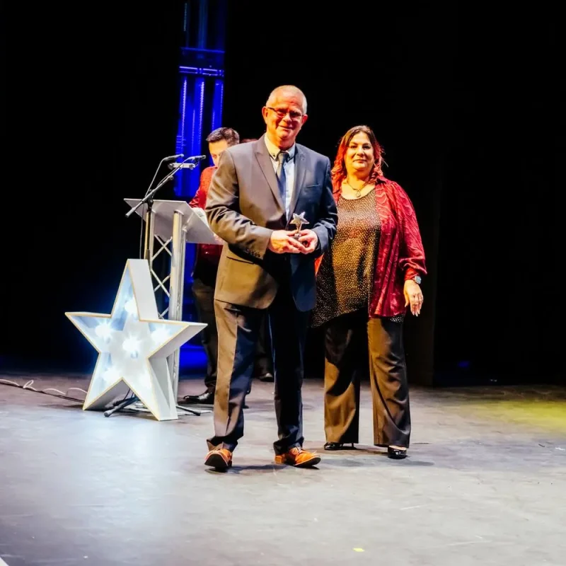 Two people on stage, one holding an award, at a college event with a star-shaped podium and a college banner.